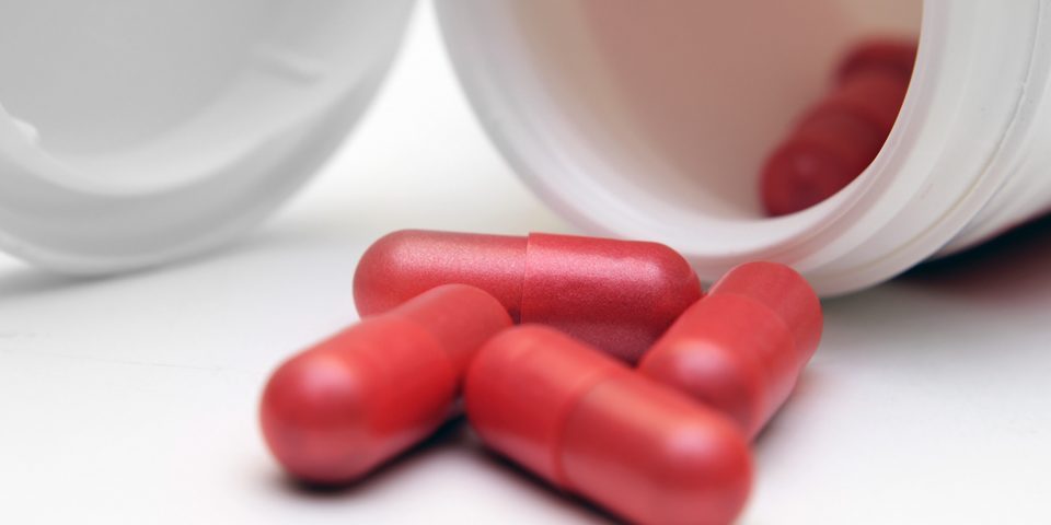 Red capsules pictured inside and outside a white bottle