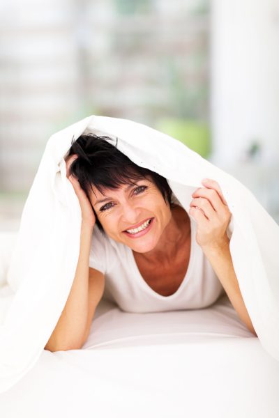 A woman lies in bed on her stomach under a white bedsheet